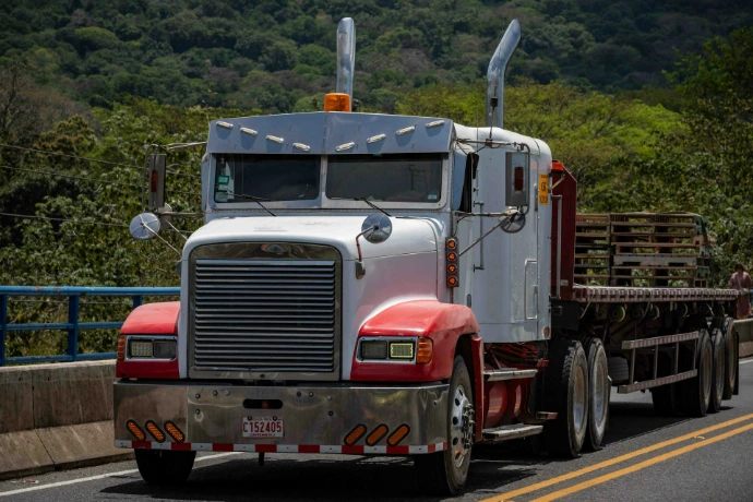 A semi truck driving down a road next to a forest